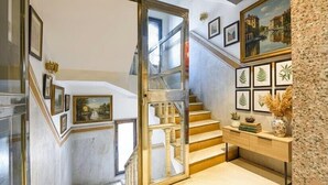 Un escalier avec une porte en verre donnant sur un niveau inférieur, entouré d’œuvres d’art encadrées et d’une console en bois.