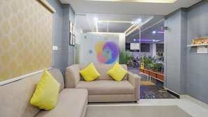 Een moderne receptiebalie met een beige bank, gele kussens en een glazen scheiding met een kleurrijk logo.