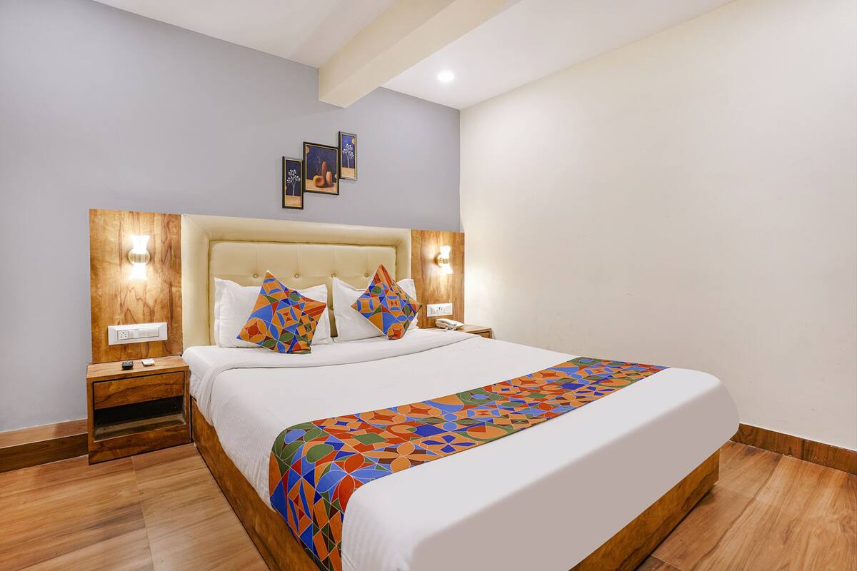Una cama bien hecha con una colcha de diseño geométrico y colores vivos, cabecera de madera y dos lámparas de noche.