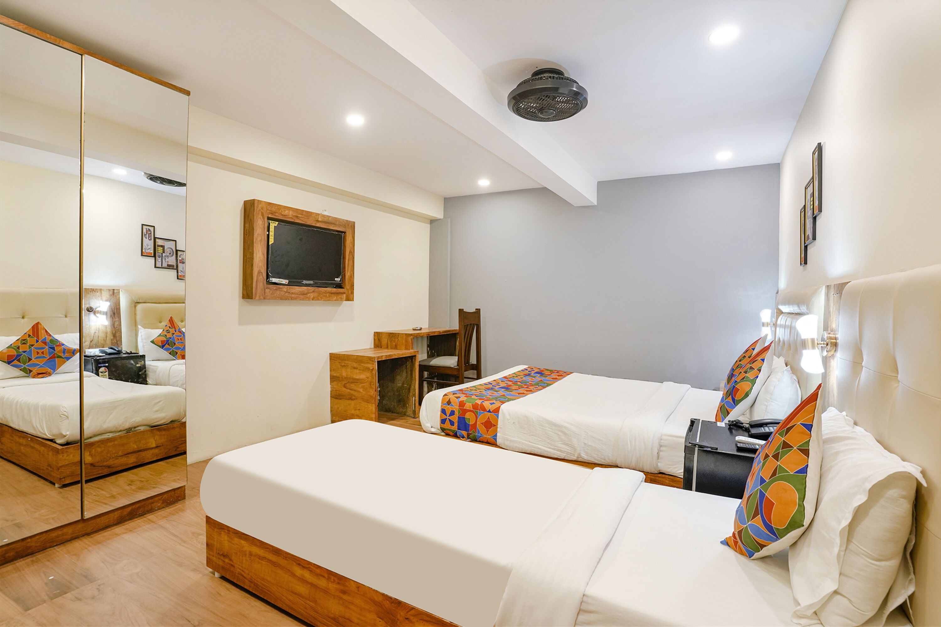 Une chambre d’hôtel avec deux lits, un bureau, une chaise, un miroir et un ventilateur de plafond.