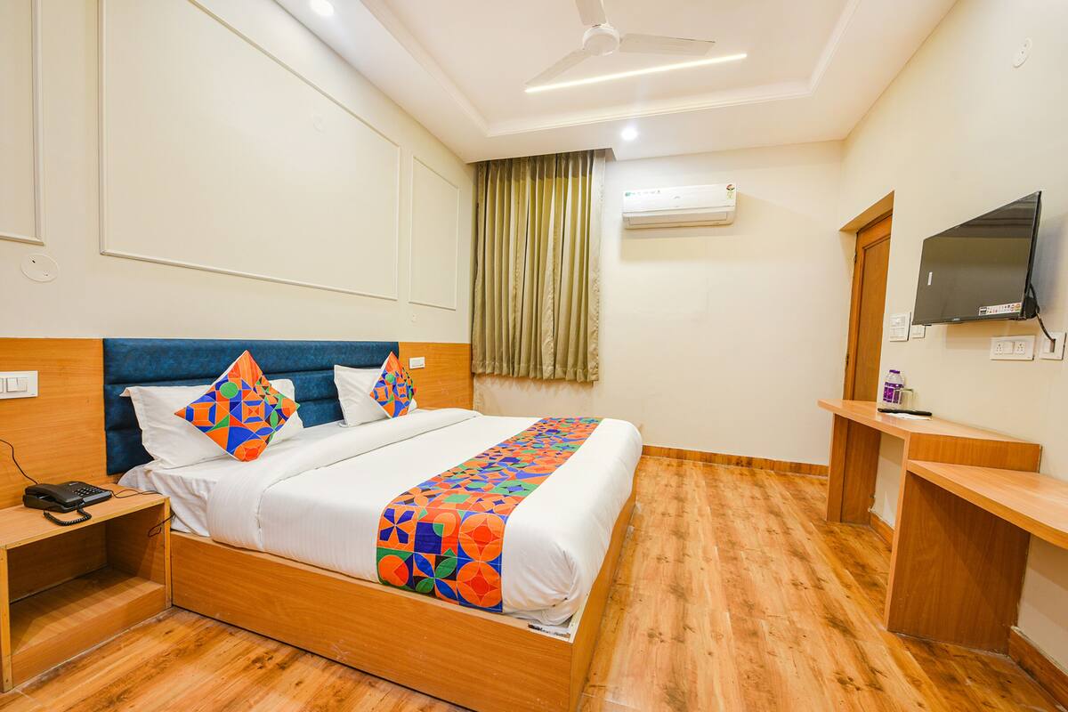 A hotel room with a wooden bed, a desk, a chair, a TV, and an air conditioning unit.