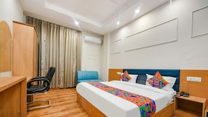 A hotel room with a wooden floor, a bed with a colorful blanket, a desk, a chair, a blue couch, and an air conditioning unit. - Fabhotel Alpine Tree (Amritsar)