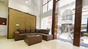 A modern hotel lobby with a sectional sofa, a glass coffee table, and a decorative wall panel. - Fabhotel Alpine Tree (Amritsar)