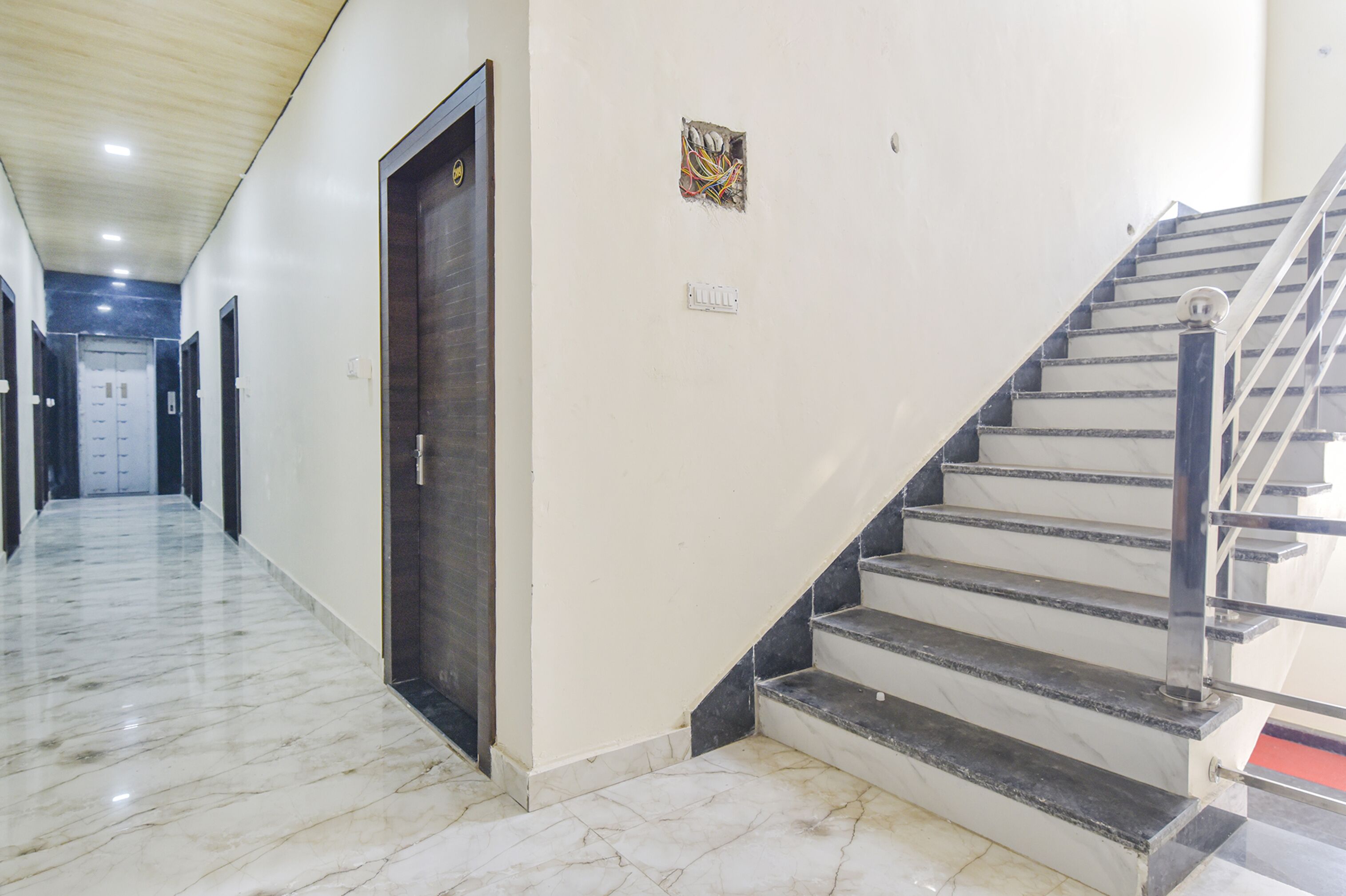 A hallway with a marble floor, a dark wooden door, a staircase with metal railings, and a wall-mounted electrical outlet.