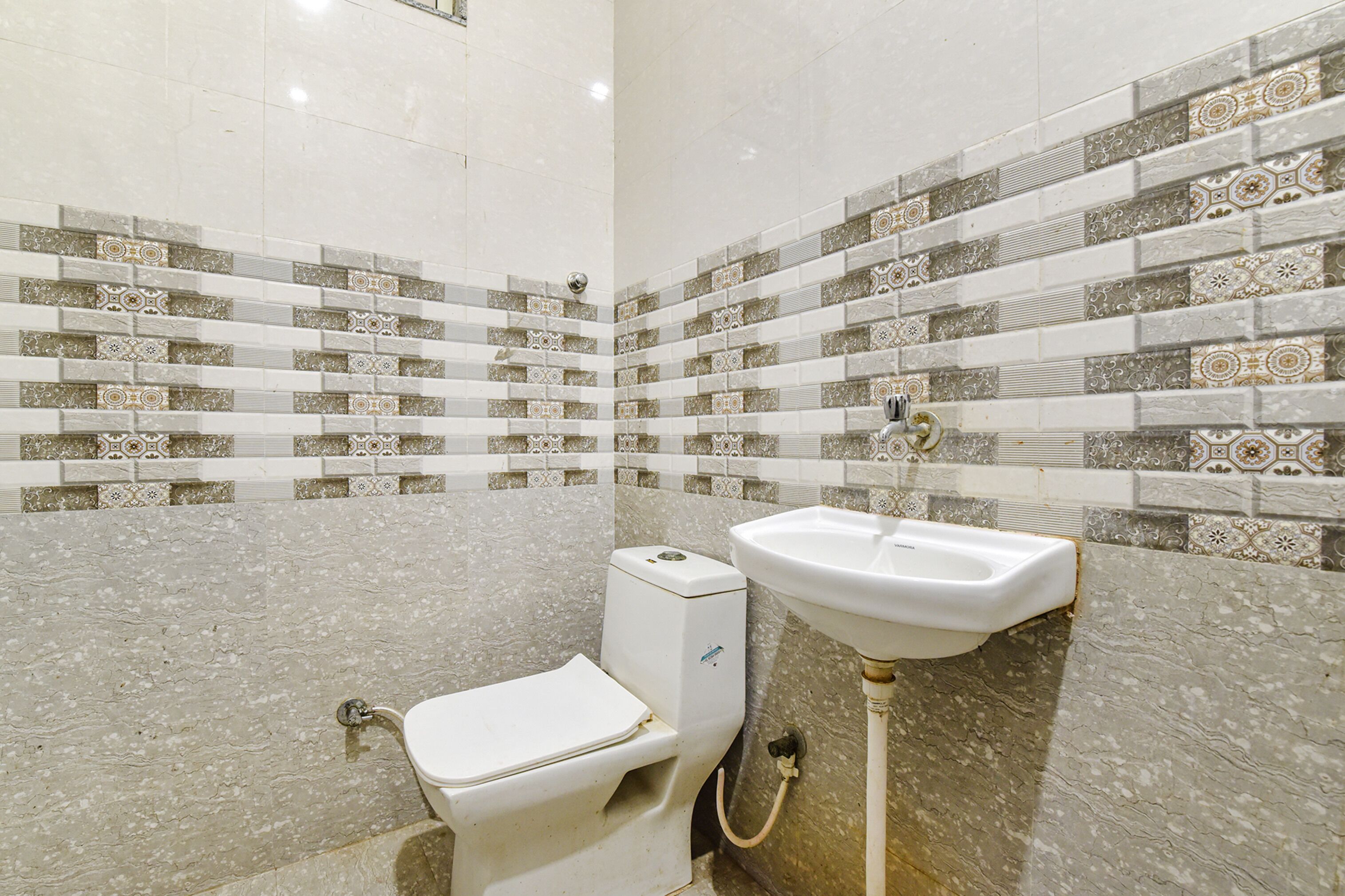 A bathroom with a toilet and sink, tiled walls, and a marble floor.