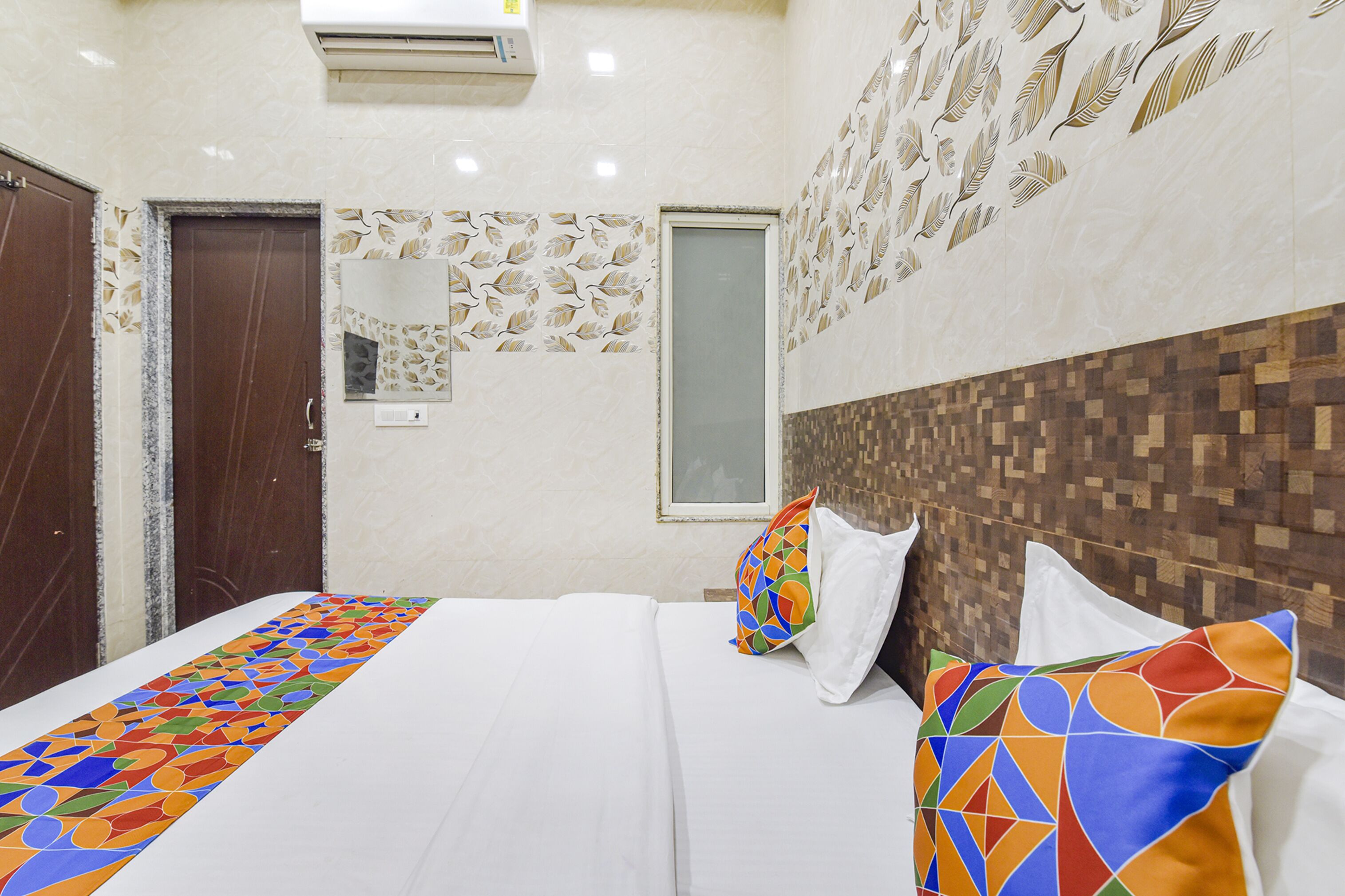 A hotel room with a bed, a mirror, a window, and a wall with a leaf pattern.