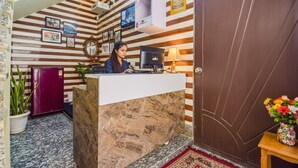 A reception desk with a marble counter, a computer, and a lamp. There are framed pictures on the wall and a door to the right. - Fabhotel Maa Gayatri Sadan (Mathura)