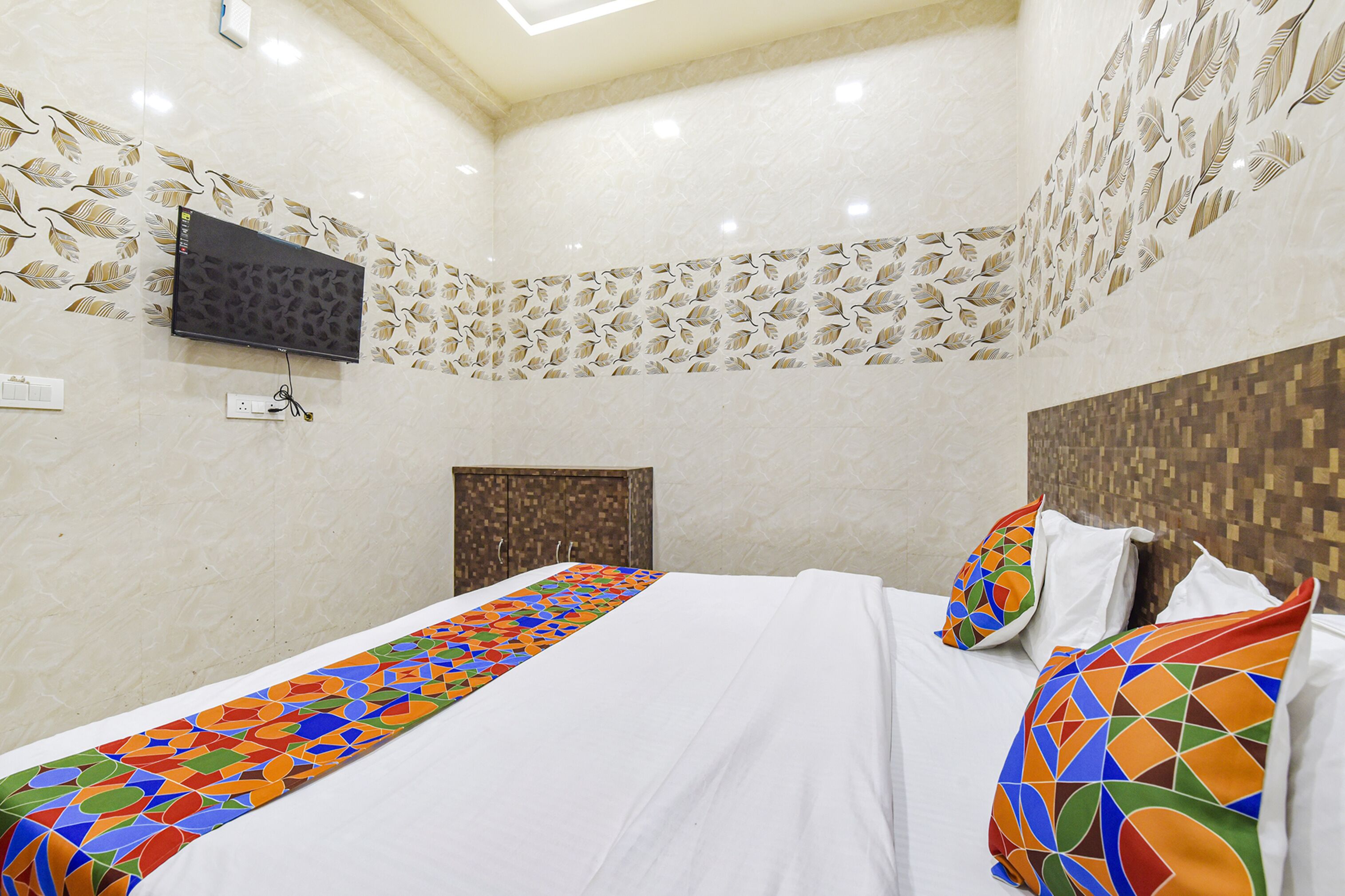A hotel room with a bed, a TV mounted on the wall, and a patterned wall design.
