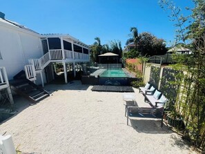 A backyard with a swimming pool, a covered patio, and outdoor seating.