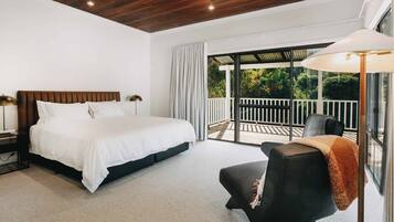 A bedroom with a large bed, a chair, a nightstand, a lamp, and a balcony with a view of greenery.