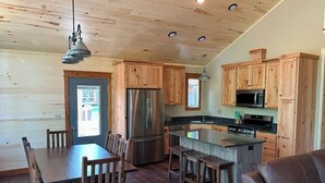 A kitchen with wooden cabinets, a stainless steel refrigerator, a stove, and a dining area with a table and chairs. - New 4-Bedroom, 2-Bath Cabin on 2,400-Acre Bay Lake – Brainerd’s Best-Kept Secret (Deerwood)