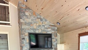 A cozy living room with a stone fireplace, leather sofa, and a TV mounted on the wall. - New 4-Bedroom, 2-Bath Cabin on 2,400-Acre Bay Lake – Brainerd’s Best-Kept Secret (Deerwood)