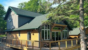 A log cabin with a deck, large windows, and a covered porch. - New 4-Bedroom, 2-Bath Cabin on 2,400-Acre Bay Lake – Brainerd’s Best-Kept Secret (Deerwood)