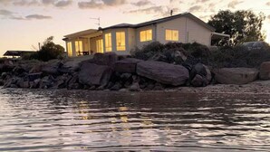 A house by a body of water with a large rock formation in front. - Absolute Beachfront Property (Fitzgerald Bay)