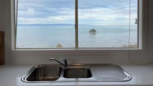 A kitchen with a double sink and a large window overlooking a body of water. - Absolute Beachfront Property (Fitzgerald Bay)