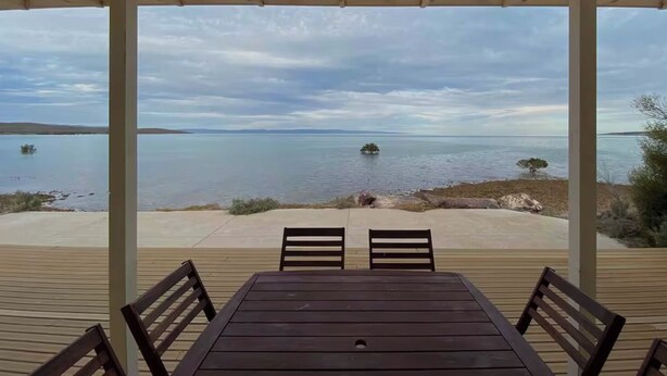 A covered outdoor seating area with a table and chairs, overlooking a calm lake with distant land and small islands. - Absolute Beachfront Property (Fitzgerald Bay)
