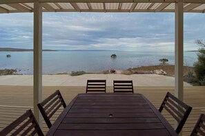 Un espace extérieur abrité, doté d’une table et de chaises, offrant une vue sur un lac paisible, avec des terres lointaines et de petites îles.