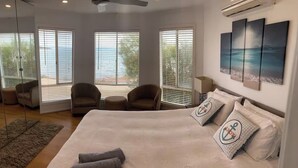 A bedroom with a large bed, two armchairs, a sofa, and a view of the sea through the windows. - Absolute Beachfront Property (Fitzgerald Bay)