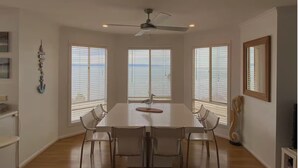 A dining area with a large table, four chairs, a ceiling fan, and large windows with blinds. - Absolute Beachfront Property (Fitzgerald Bay)