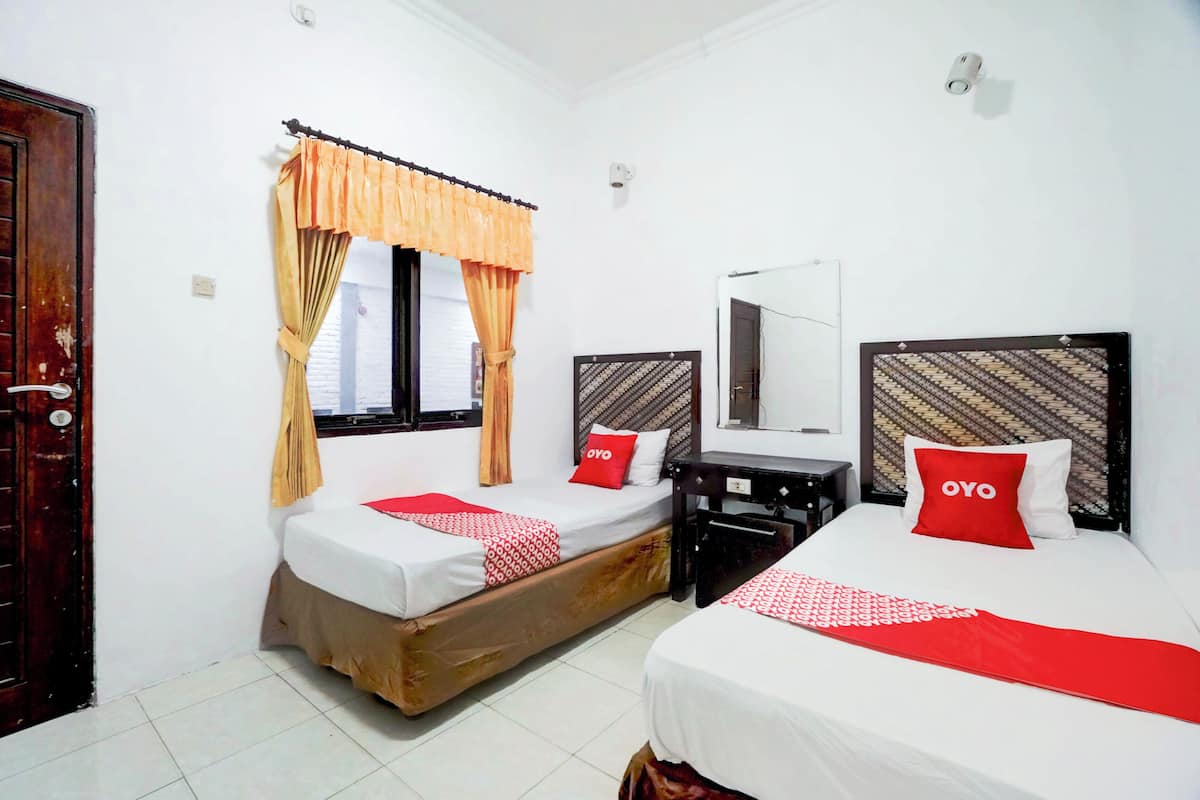 A hotel room with two single beds, a desk, and a mirror.