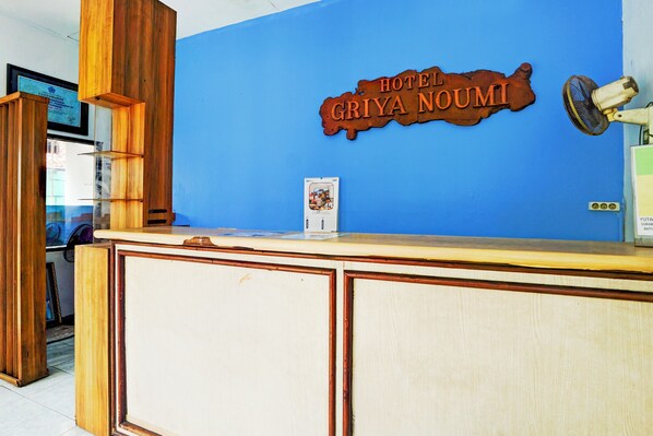 A reception desk with a wooden design, a blue wall, and a sign that reads "HOTEL GRIYA NOUMI". - Hotel O Bungurasih Near Juanda International Airport Formerly Griya Waru Hotel (Surabaya)