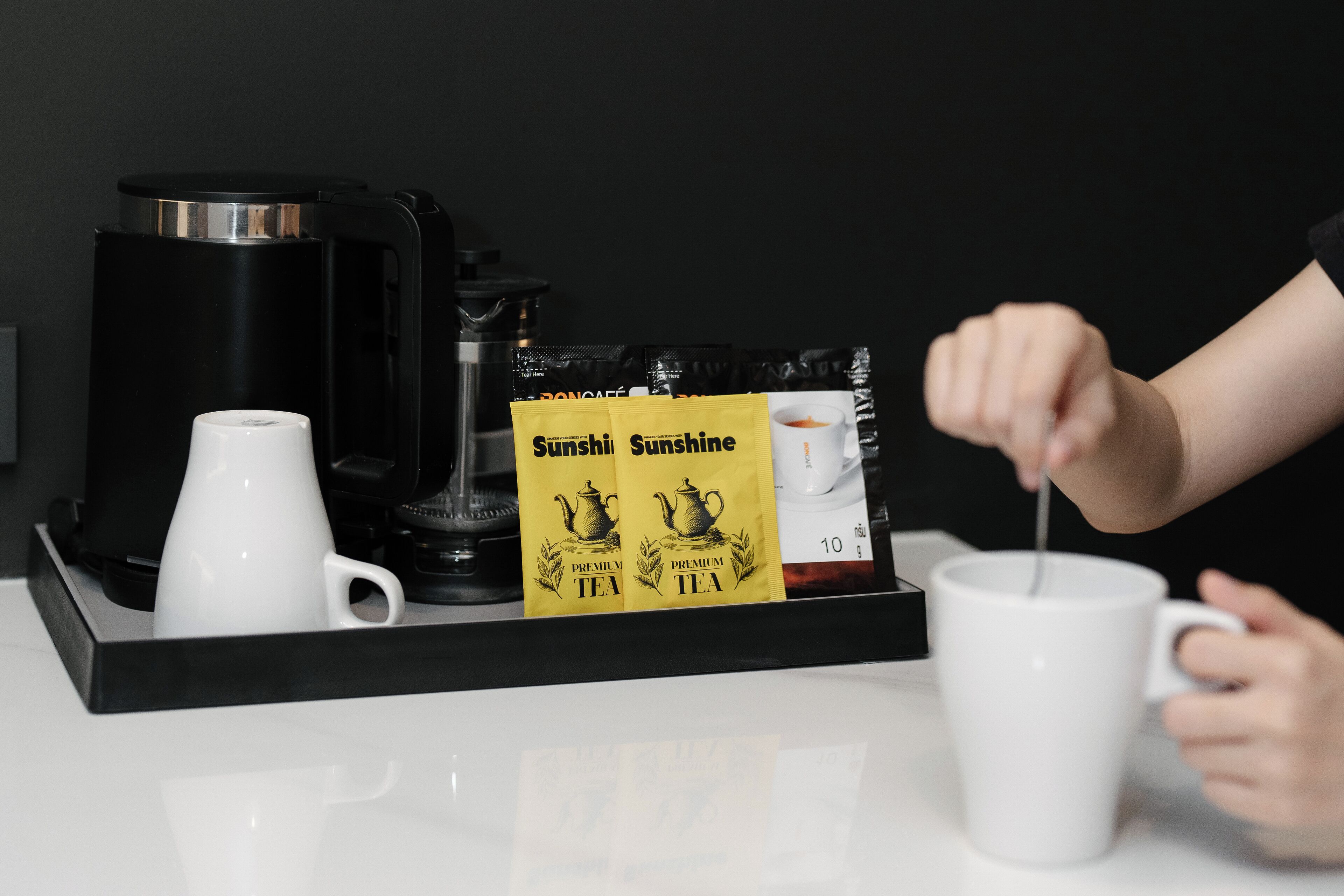 A coffee machine, a white mug, and tea packets on a tray.