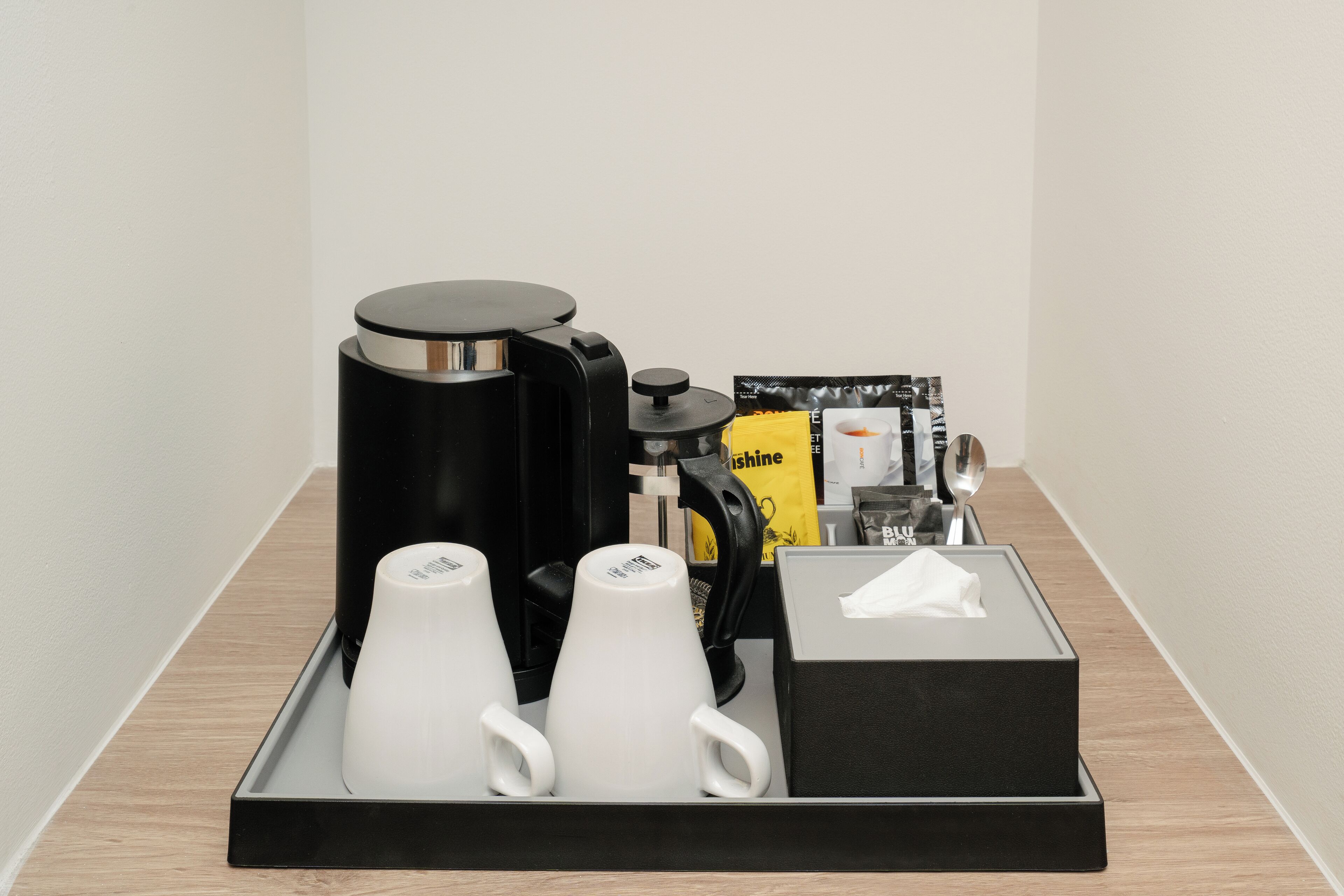 Un plateau contenant une machine à café, deux tasses blanches, une boîte de mouchoirs et un paquet de dosettes de café.
