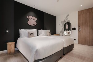 Un dormitorio moderno con dos camas, un taburete pequeño de madera y un espejo grande en la pared.