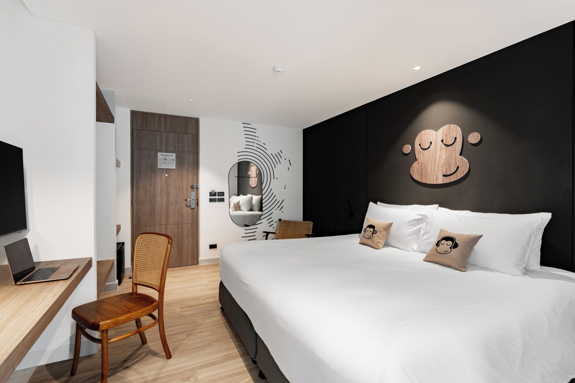 A modern hotel room with a large bed, a desk with a laptop, and a chair.