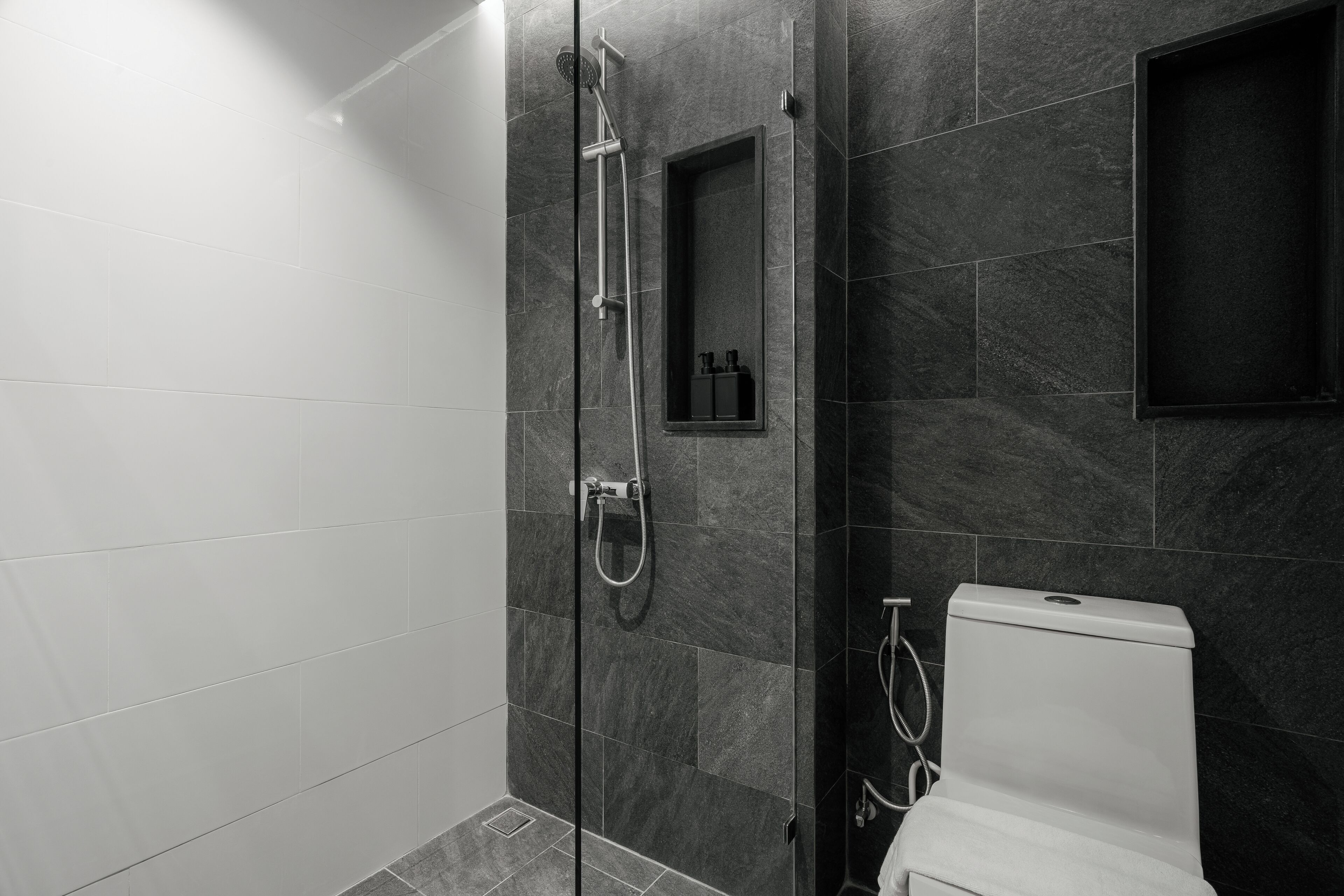 A modern bathroom with a glass-enclosed shower, a toilet, and a small shelf with toiletries.
