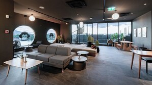 A modern lounge area with a sofa, round tables, and a staircase leading to a balcony with a view. - Blu Monkey Hub & Hotel Bangtao Beach Phuket (Choeng Thale)