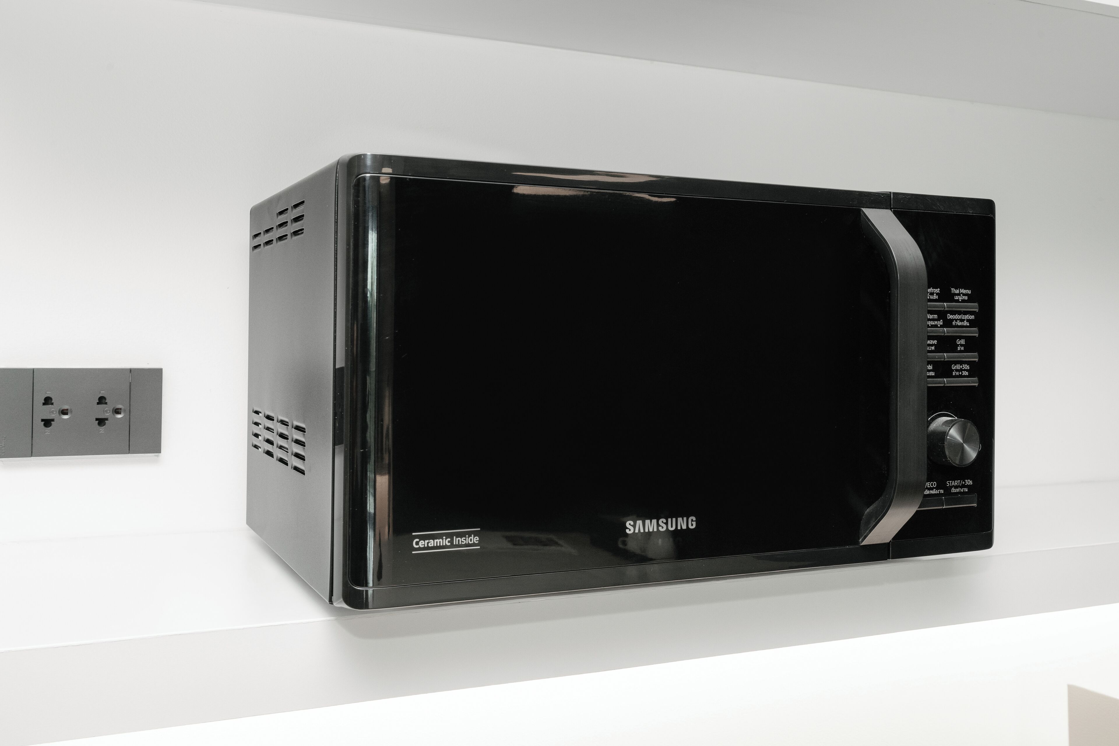 A black Samsung microwave oven with a control panel on the right side, mounted on a white wall.