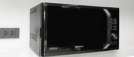 A black Samsung microwave oven with a control panel on the right side, mounted on a white wall.