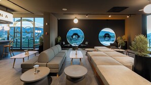 A modern lounge area with sofas, round tables, and large windows offering city views. - Blu Monkey Hub & Hotel Bangtao Beach Phuket (Choeng Thale)