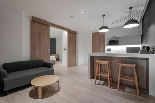 A modern kitchen with wooden accents, a dark grey sofa, and two wooden stools.