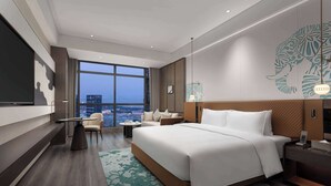 Une chambre d’hôtel moderne dotée d’un grand lit, d’un coin salon avec un canapé et des fauteuils, d’une petite table et d’une grande fenêtre donnant sur la ville.
