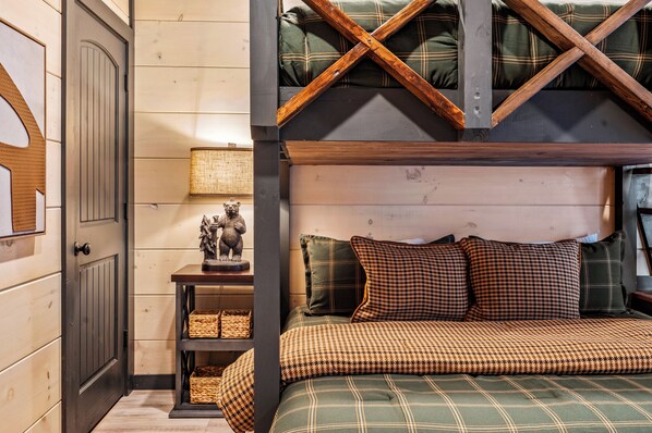 A cozy bedroom with a bed, wooden beams, a lamp, and a shelf with baskets.