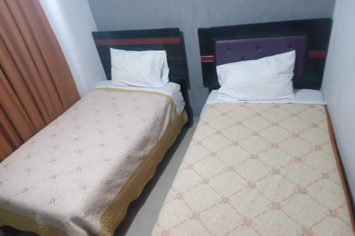 Two single beds with headboards, a brown curtain, and a patterned bedspread.