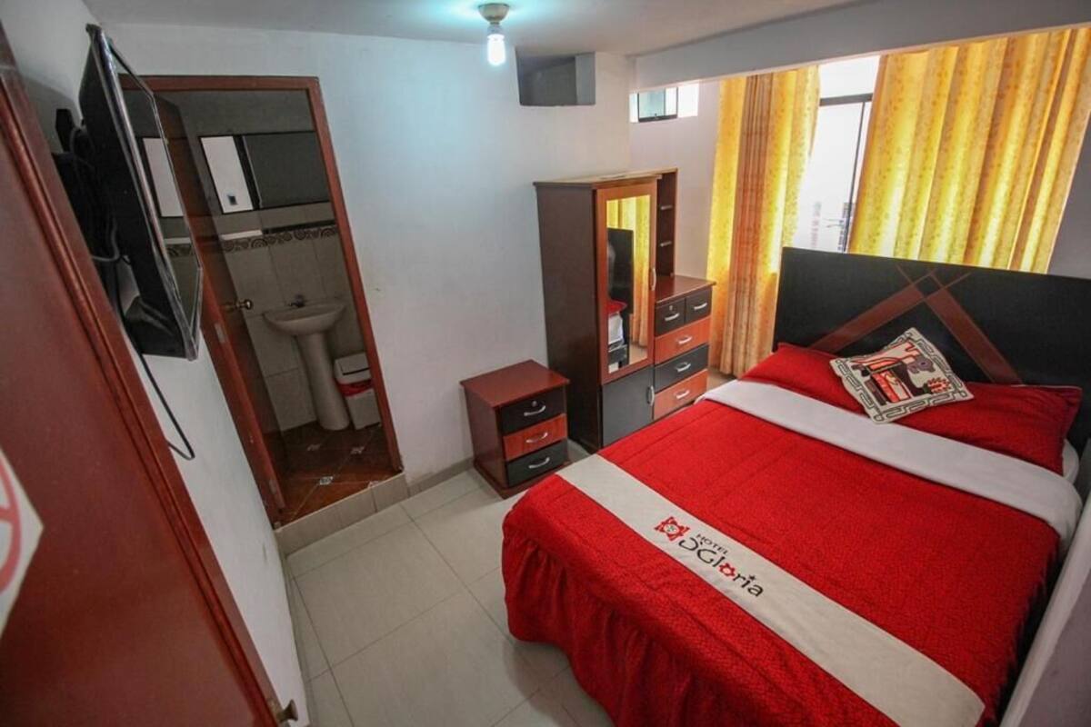 A hotel room with a bed, a wardrobe, a mirror, a sink, and a door leading to a bathroom.
