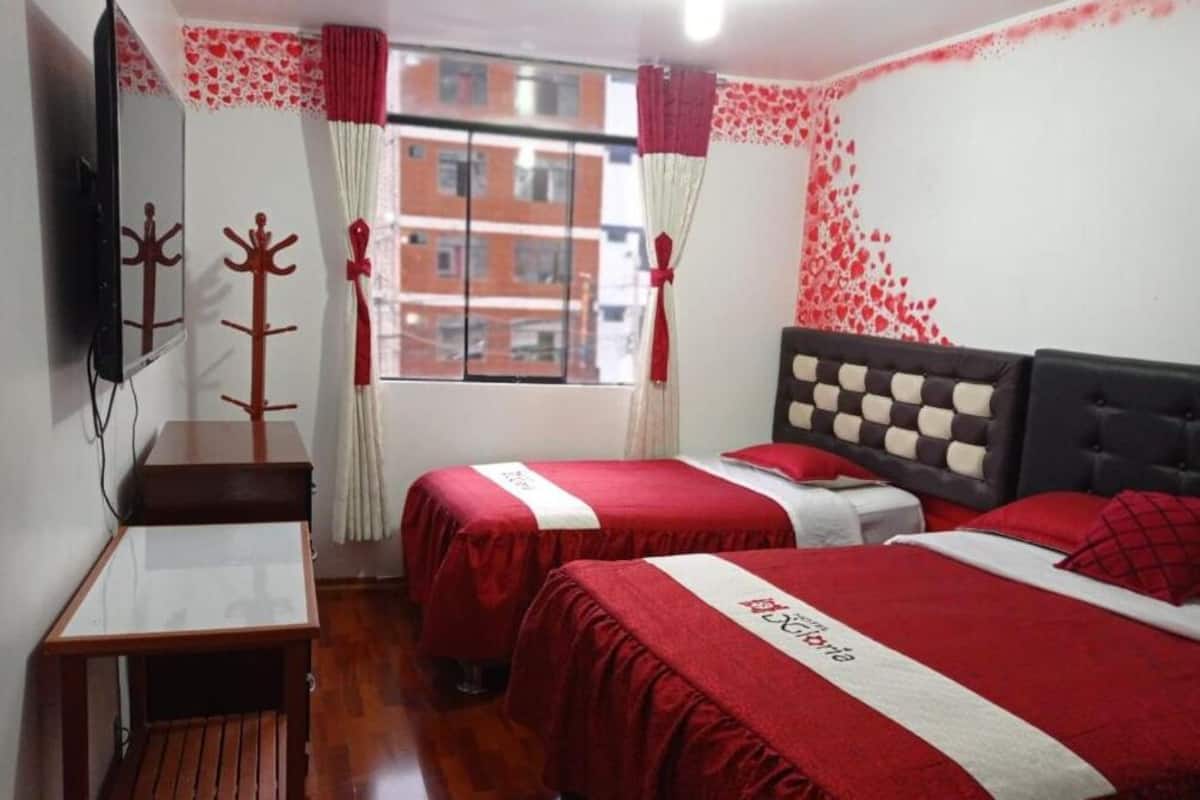 A hotel room with two beds, a small table, a TV, and a window with curtains.