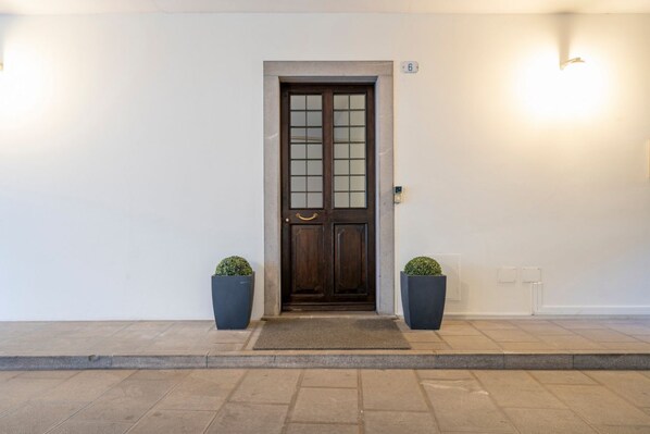 A dark wooden door with glass panels, flanked by two potted plants, and a number '6' sign above it.