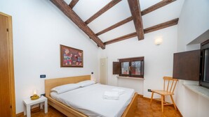 Quarto com cama de madeira, mesa de cabeceira, cadeira, janela e um quadro na parede.
