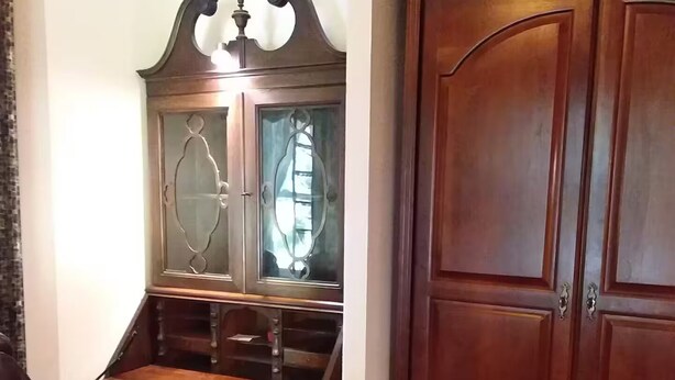 Un escritorio de madera tradicional con una silla, un aparador con puertas de vidrio y un estante superior.