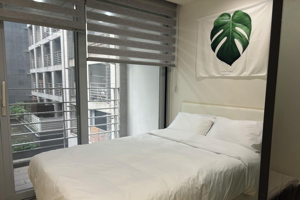 Een slaapkamer met een groot bed, een raam met zonwering en een poster met een groen blad aan de muur.