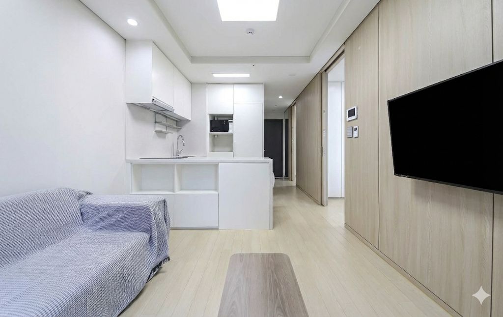 A modern living space with a sofa, a flat-screen TV mounted on a wall, and a kitchenette area.