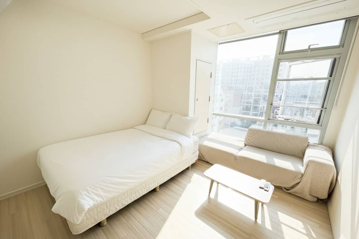 Een moderne slaapkamer met een bed, een bank, een kleine tafel en een groot raam met uitzicht op de stad.