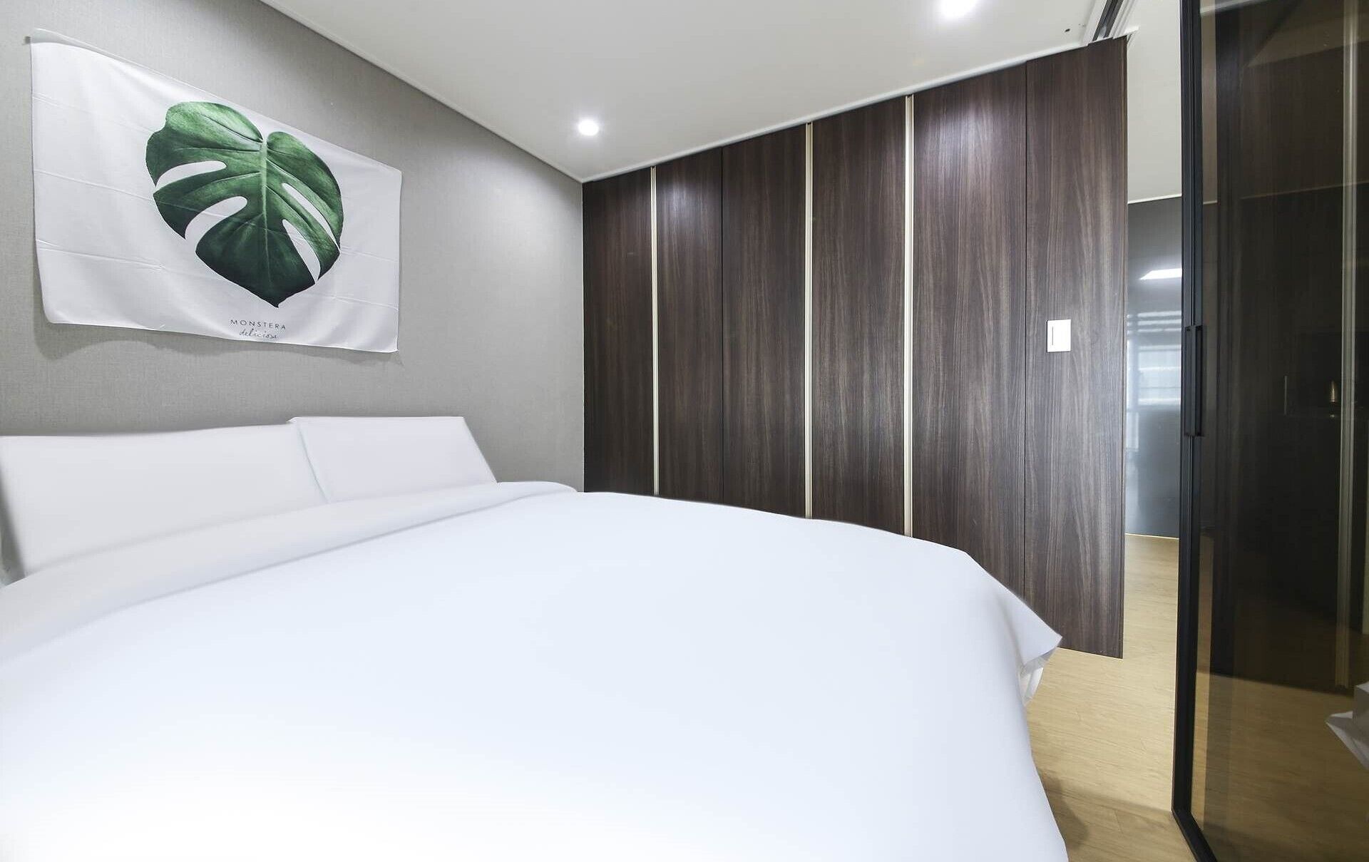 A bedroom with a large bed, a wardrobe, and a glass door leading to a bathroom.