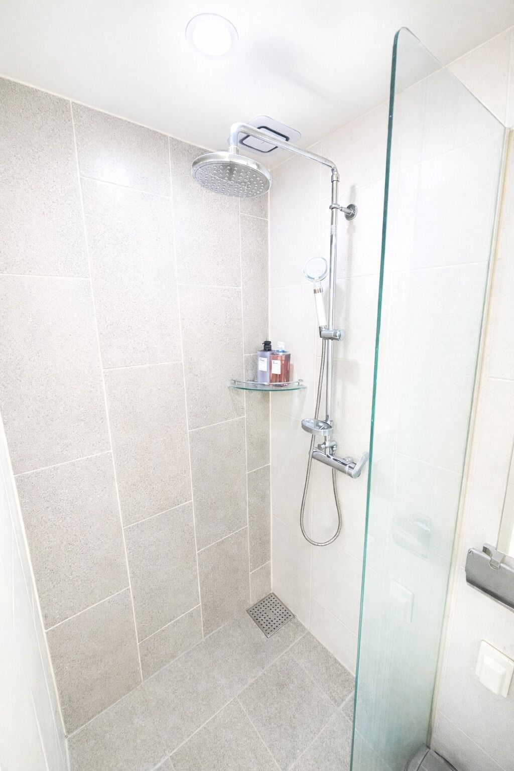 A modern shower with a glass door, a handheld showerhead, and a handheld shower attachment.