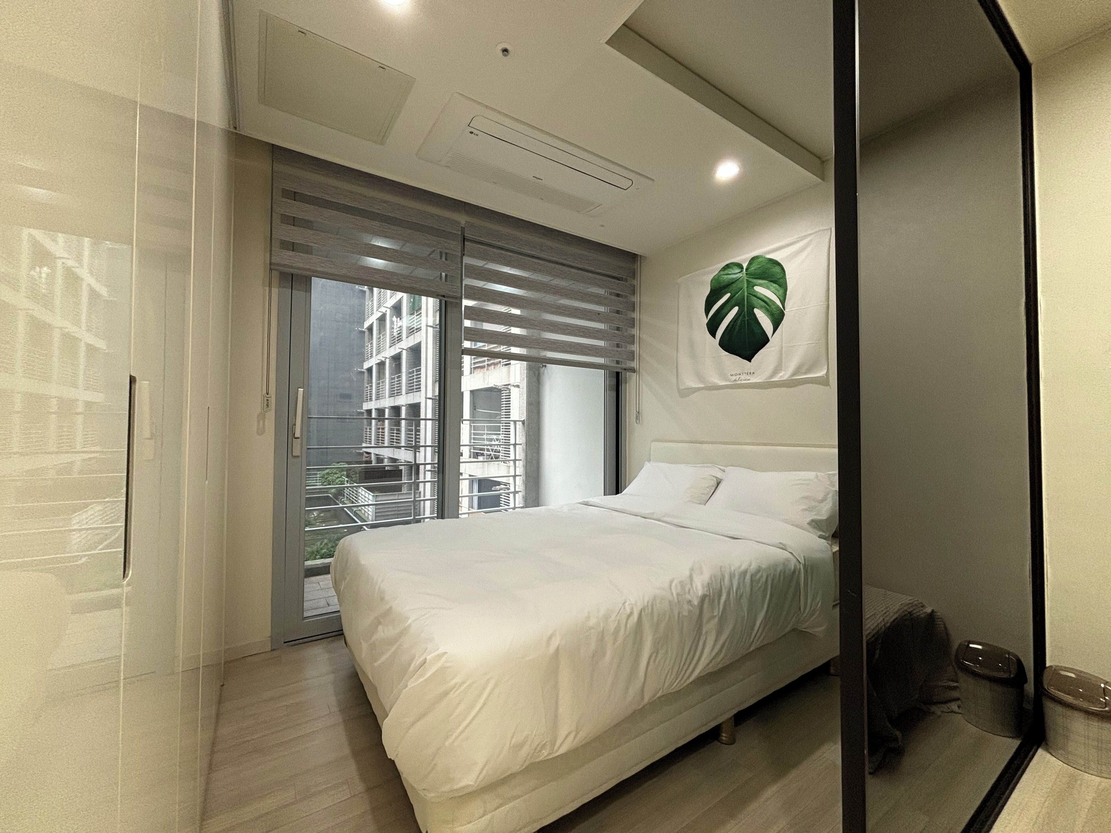 A modern bedroom with a large bed, a sliding glass door leading to a balcony, and a wall-mounted plant.