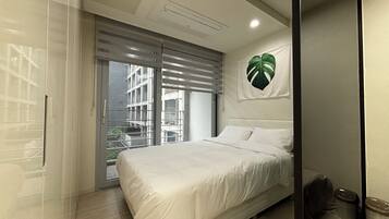 A modern bedroom with a large bed, a sliding glass door leading to a balcony, and a wall-mounted plant.